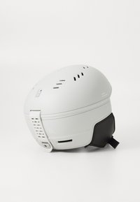 Biely lyžiarsky prilba s ventilačnými otvormi, s hladkým matným povrchom a čiernou bradou. Obsahuje nastaviteľné popruhy a logo na boku.