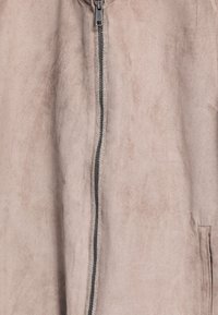 Lichtroze suedeblauwe jas met een rits over de hele lengte, een gladde textuur en zijzakdetails, die subtiele kleurvariaties laat zien.
