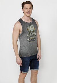 Szürke ujjatlan felső koponya grafikával és virágos részletekkel, felgöngyölt kék farmer nadrággal párosítva. Kényelmes fazon, puha anyag és nyomtatott minta.