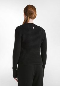 Schwarzer gerippter Pullover mit langen Ärmeln, der horizontale Streifen aufweist. Rückendetail mit einem kleinen rosa Etikett am Kragen.