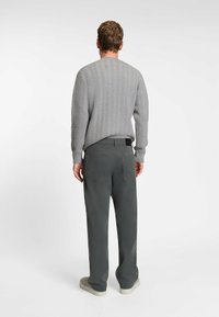 Hellgrauer gestrickter Pullover mit einem strukturierten Fischgrätenmuster, kombiniert mit dunkelgrauen geraden Hosen und beigen Sneakers.