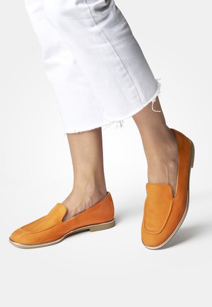 Orange leather slip-on shoes with a rounded toe, featuring a subtle stitch detail and a slim white sole. Worn with white cropped pants.