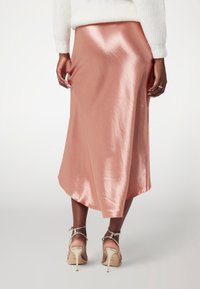 Rožinė satino vidutinio ilgio sijonas su aukštos ir žemos linijos hemu, glotnia tekstūra ir subtiliu blizgesiu. Suderintas su dirželių aukštakulniais.