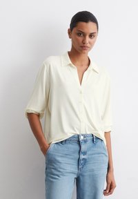 Lys gul skjorte med krage, avslappet passform, oppbrettede ermer og en glatt tekstur, sammen med lyseblå denimjeans.