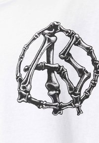 Valkoinen puuvillapaita, jossa on musta graafinen design, johon on järjestetty luuston kuvioita "A"-muotoon. Painatus sisältää yksityiskohtaisen tekstuurin ja varjostuksen.