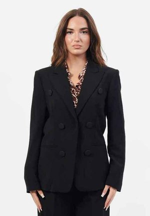Blazer doppiopetto nero in tessuto testurizzato, con bottoni rotondi e spalle strutturate. Indossato sopra una blusa a fantasia.