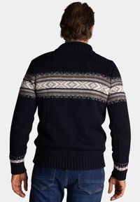 Marineblauwe gebreide trui met een fair isle patroon in wit en beige, voorzien van een geribde kraag en manchetten, en een gestructureerde brei-afwerking.