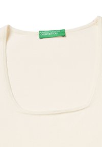 Krémově zbarvené tílko s širokým čtvercovým výstřihem, jemnou texturou a zakončenými okraji; nese zelenou etiketu s nápisem "UNITED COLORS OF BENETTON".