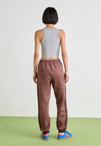 Šedý krátký top na ramínka, hnědé tepláky s černými bočními pruhy a modré sportovní boty s červenými akcenty. Hladká textura a neformální design.