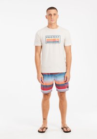 Beige T-shirt voor heren met een bedrukte logo en strepen. Kleurvolle gestreepte zwembroek in tinten blauw, rood en oranje, en slippers.