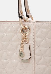 Roze gewatteerde handtas met glanzende afwerking, voorzien van goudkleurige hardware, dubbele riemen en een decoratieve bedel met logo.