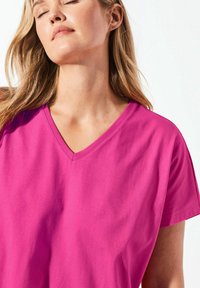 V-Ausschnitt-T-Shirt in leuchtendem Pink, gefertigt aus weicher Baumwolle. Kurze Ärmel mit lockerer Passform, versehen mit einer glatten Textur und einfachem Design.