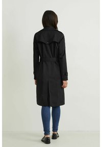 Czarny płaszcz typu trench z paskiem w talii, tylnym klapem i zapinanymi mankietami. Nosi się go na niebieskie dżinsy i czarne buty, pokazany z tyłu.