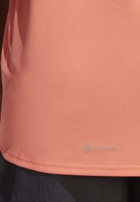 Gros plan d'un tissu texturé couleur pêche avec un petit logo imprimé indiquant "Aeroready" près du bord inférieur.