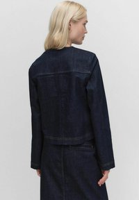Veste en denim foncé au design court, avec manches longues, détails de couture et ourlet droit. Texture lisse, matériel minimal.