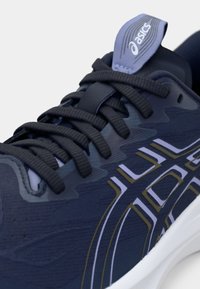 Zapatilla de correr de color azul marino con un upper texturizado, que presenta cordones oscuros, una lengüeta azul claro y una suela blanca con acentos en dorado y blanco.