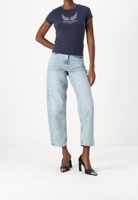 T-shirt blu navy a maniche corte con design grafico bianco, abbinato a jeans dritti a vita alta di colore azzurro chiaro e scarpe nere con tacco e accenti metallici.