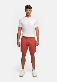 Hvit bomull T-skjorte for menn med lomme og korallfargede shorts med snøring, sammen med hvite joggesko. Enkel design og avslappet passform.