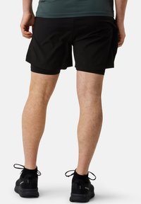 Zwarte sportieve shorts gemaakt van lichte stof, met een elastische tailleband. Gecombineerd met zwarte sportieve schoenen met veters.