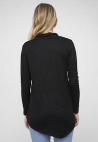 Zwart top met lange mouwen van een zacht, lichtgewicht stof met een afgeronde zoom en een col ontwerp, gedragen met een blauwe spijkerbroek.