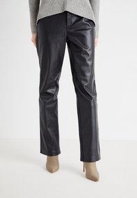 Zwarte leren broek met een slim fit, met een gladde textuur en een recht model, gecombineerd met beige puntige hakken.