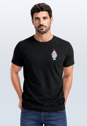 Man with short curly hair and beard wearing a black t-shirt with a small white fish graphic and red bottle cap on the chest.