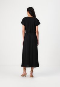 Black maxi dress with short sleeves and an elastic waist. Smooth fabric, ankle-length, paired with tan strappy high-heeled sandals.