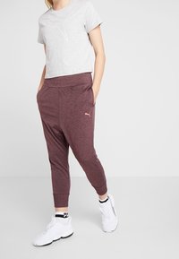 Graues, kurzes T-Shirt mit weißem Logo, kombiniert mit burgunderfarbenen, tapered Jogginghosen mit Seitentaschen und kleinem pinken Logo, getragen mit weißen Sneakers.