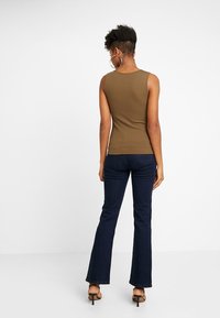 Olivgrön ribbad linne med en figurnära design, bärs tillsammans med mörkblå utsvängda jeans. Outfiten kompletteras av öppetåiga klackar.