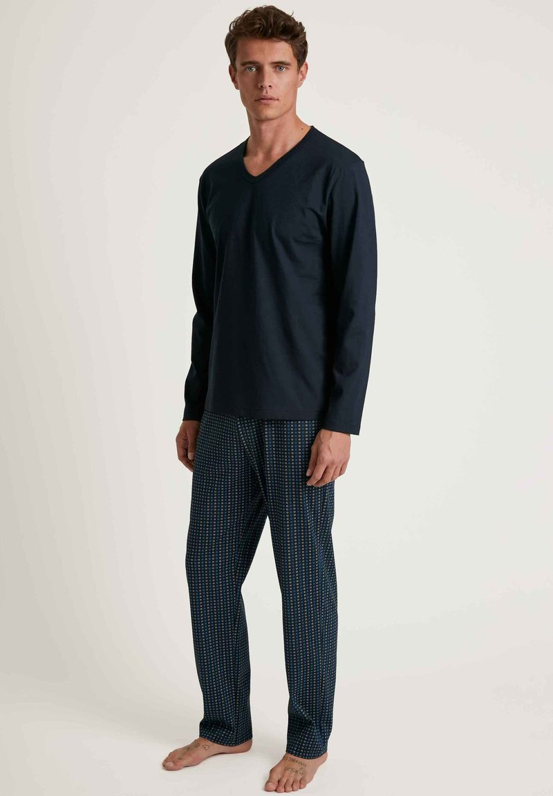Haut à manches longues bleu marine, à col en V, associé à un pantalon de pyjama à motifs avec des pois bleu clair sur fond sombre. Matière en coton, coupe décontractée.