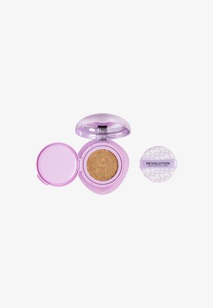Compact lavande ouvert avec un fond de teint cushion beige à l'intérieur, à côté d'une éponge applicatrice ronde étiquetée « Revolution ».