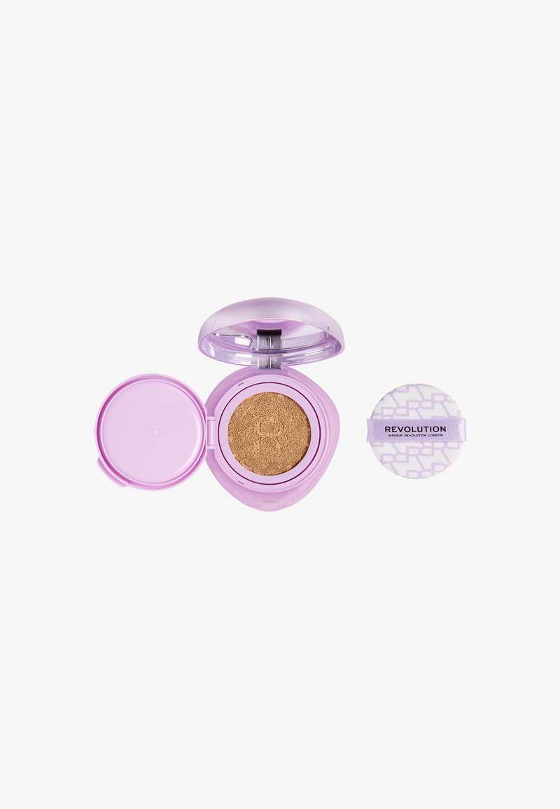 Compact lavande ouvert avec un fond de teint cushion beige à l'intérieur, à côté d'une éponge applicatrice ronde étiquetée « Revolution ».