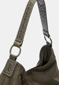 Cinghia per borsa a mano in suede verde con grandi ritagli circolari, dettagli in hardware metallico e cuciture a contrasto.