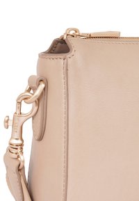 Borsa a mano in pelle beige con texture liscia, hardware dorato e chiusura con zip. I dettagli includono cuciture e un attacco a clip.