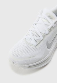 Baskets blanches en matériau en mesh avec des accents réfléchissants et un design texturé ; comportent des lacets et un logo Nike.