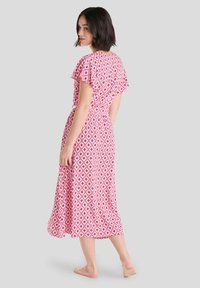 Vestido midi rosa con un patrón geométrico de diamantes en blanco, mangas cortas acampanadas y diseño de cintura fruncida. Textura de tela suave.