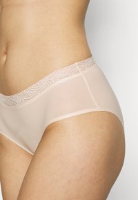 Culottes pour femmes en rose clair, fabriquées dans un tissu lisse. Présentent une taille en dentelle avec un motif décoratif et des côtés sans couture pour plus de confort.