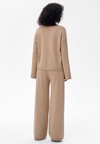 Beige gebreide loungewear set met een loszittende trui met verslapte schouders en wijde broekspijpen; zachte textuur met een subtiele glinstering.