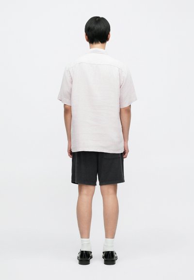 Πουκάμισο από λινό, ανοιχτό ροζ με κοντά μανίκια και απλό σχεδιασμό, συνδυασμένο με σκουρόχρωμα, μαλακά σορτς και μαύρα παπούτσια, από πίσω.