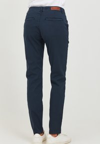 Marineblå slim-fit bukser laget av bomull, med en brun skinnlapp i livet og to baklommer. Stilig med tapered ben.