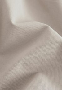 Tissu beige clair avec une surface texturée, présentant un motif côtelé subtil et des plis lisses et drapés.