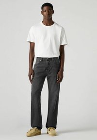 Jeans in denim nero con vestibilità dritta, finitura testurizzata e design a cinque tasche, abbinati a una t-shirt girocollo bianca semplice e mocassini beige.