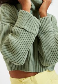 Maglione verde a coste con collo alto e maniche oversize, dotato di un design cropped e tessuto testurizzato.