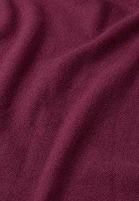 Tessuto morbido al tatto di un profondo bordeaux con pieghe sottili e un motivo a maglia leggermente rialzato.