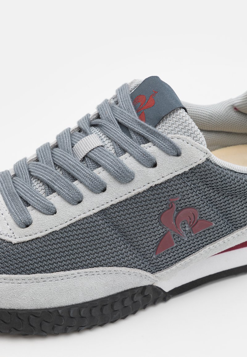 Baskets en tissu gris avec maillage texturé et accents en daim. Caractéristiques des lacets gris, un logo rouge et une semelle en caoutchouc noire pour l'adhérence.