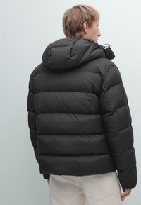Giacca a vento nera con cappuccio, design trapuntato e coulisse elastica. Leggera, con una superficie liscia e una vestibilità aderente.