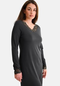 Robe à manches longues de couleur gris foncé avec un design en V et des accents en dentelle au niveau de l'encolure et des poignets, mettant en valeur une texture lisse.