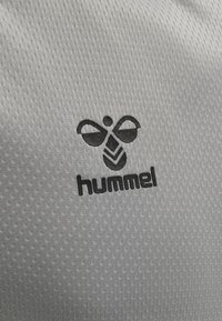 Grå tekstureret stof med et sort bi-logo over teksten "hummel" i fed, versaler. Designet fremhæver enkelhed og kontrast.