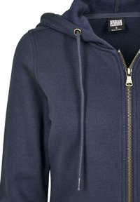 Sweat à capuche zippé marine en tissu doux ; possède une capuche avec cordon de serrage, une fermeture éclair dorée et des poches latérales. Surface texturée.