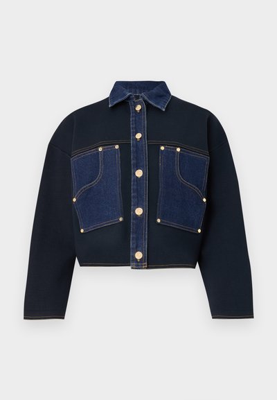 Chaqueta recortada con tela de color azul oscuro y bolsillos frontales de mezclilla. Botones dorados acentúan el centro y los bolsillos. Cuello clásico y corte suelto.